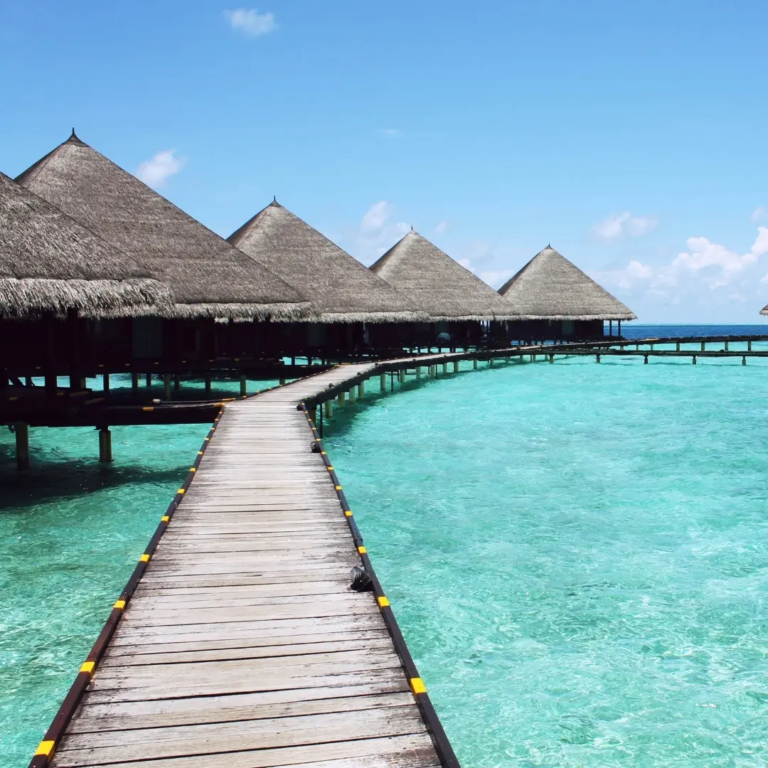 Overwater bungalows reached by a wooden walkway above clear turquoise water