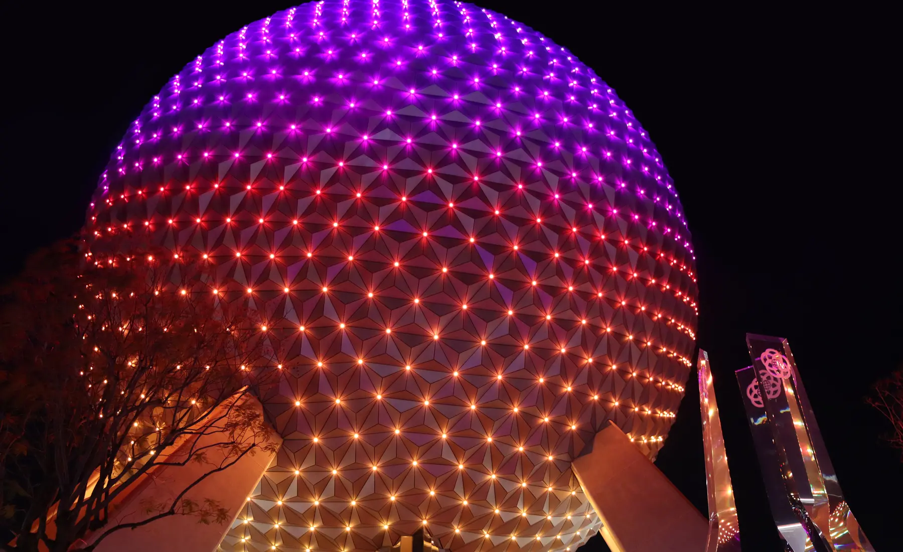 Spaceship Earth glowing in rich pink and violet light after dark